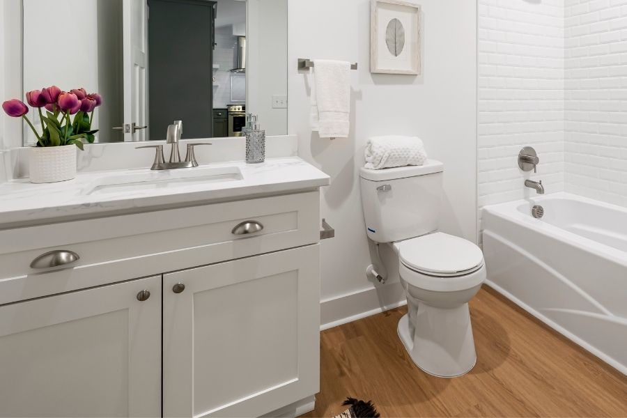A clean, modern bathroom featuring a white vanity with a marble top, a white toilet, and a bathtub with white subway tile.