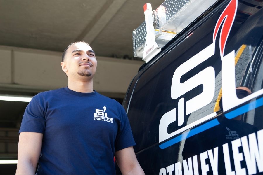 A service technician in a navy blue company t-shirt looking upward while standing next to a branded service vehicle.
