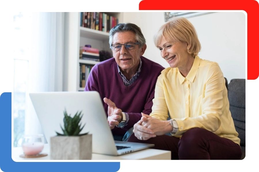 An older couple smiling and talking while looking at a laptop screen together in a living room