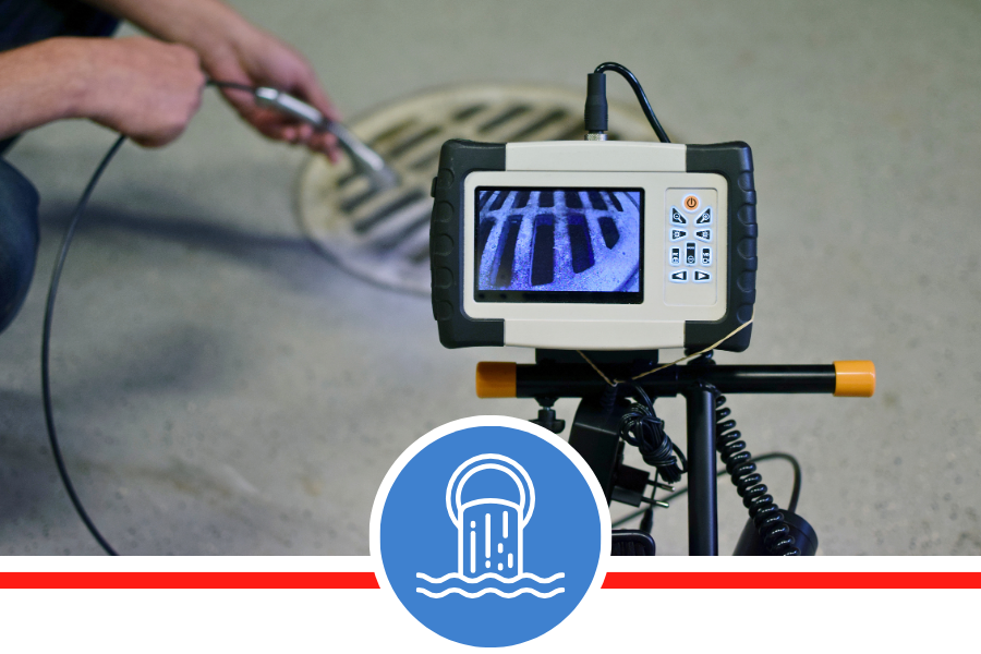 A digital monitor showing a live camera feed of the inside of a sewer pipe, with a technician holding a cable in the background.