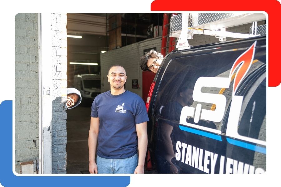 Three coworkers in matching navy blue company t-shirts posing playfully by a service van and an open garage door.